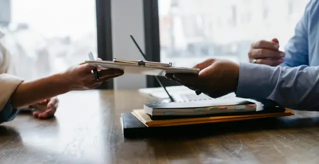 Close-up of man in a suit passing clipboard to employer